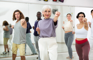 Fototapeta premium Portrait of smiling determined elderly woman practicing basic punches during group self defense course