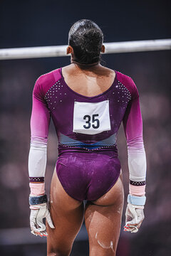 An elegant, muscular black gymnast from the back, wearing a number 35 just before she entered the uneven bars or asymmetric bars competition