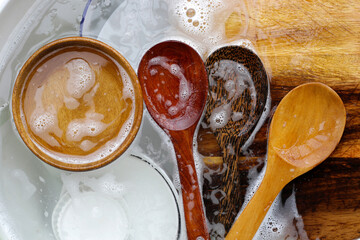 Wooden spoon, cutting board and dishes in water and bubbles of dishwashing liquid - obrazy, fototapety, plakaty