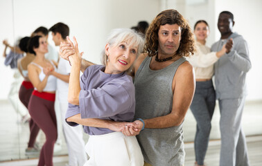 Obraz premium Happy caucasian guy and old lady practising paired latin dance in dance studio
