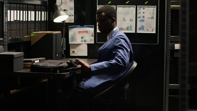 Arriving at workplace, black man with experience in criminal investigation opening his minicomputer. African american investigator sitting in workroom with laptop bag, ready to conduct study.