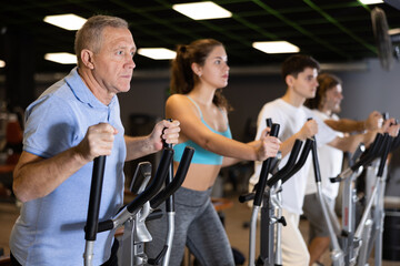 Focused aged man leading healthy active lifestyle doing cardio workout on elliptical machine in modern gym