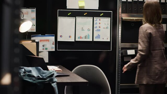 Caucasian female inspector conducting investigation in incident room, analyzing evidence and reviewing statements. Surrounded by case files and using laptop for research. Committed to justice.