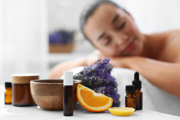 Woman relaxing on massage couch and bottles of essential oil with ingredients on table in spa...