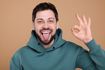 Happy man showing his tongue and making ok gesture on beige background