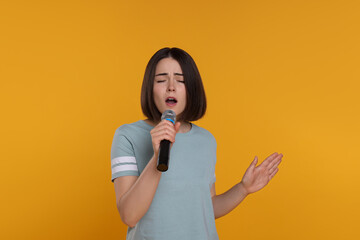 Beautiful young woman with microphone singing on yellow background