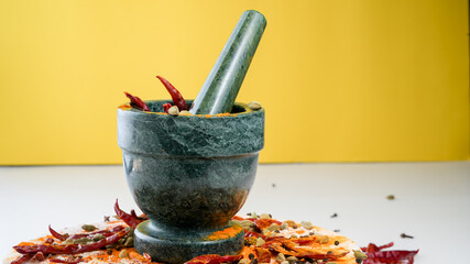 Granite mortar and pestle with colorful  spices with yellow background and copy space