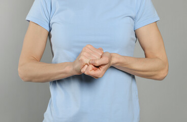 Woman cracking her knuckles on light grey background, closeup. Bad habit