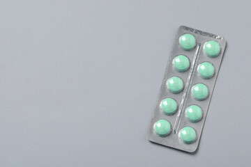 Green pills in blister on grey background, top view. Space for text