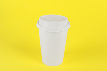 Paper cup with plastic lid on yellow background. Coffee to go
