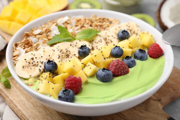Tasty matcha smoothie bowl served with fresh fruits and oatmeal on table, closeup. Healthy breakfast