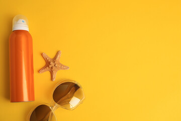 Bottle of sunscreen, starfish and sunglasses on yellow background, flat lay. Space for text