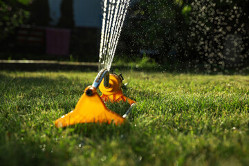 Automatic sprinkler watering green grass on sunny day outdoors. Irrigation system