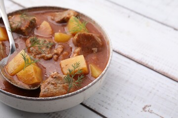 Delicious goulash in bowl on white wooden table, closeup. Space for text