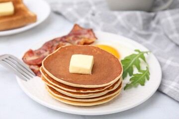 Tasty pancakes served with fried egg and bacon on white table