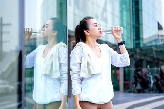 slim Asian woman runner drinking water from water bottle in sunny at city.Healthy and active lifestyle concept.