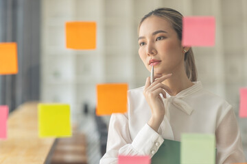 business asian girl in white shirt thinks, holds pen and clipboard, writing sticking adhesive notes...