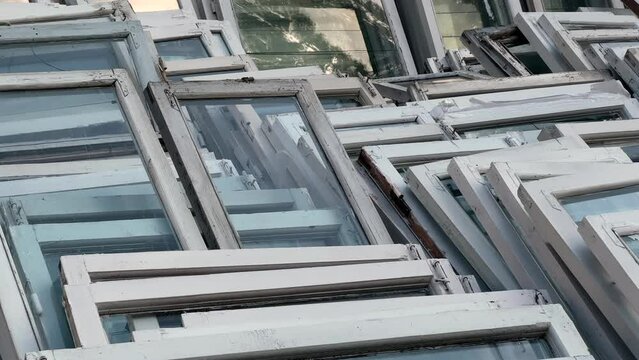 Old wooden windows lie in a pile near the building after being replaced with modern double-glazed windows. Long angle view