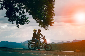 couples wearing safety helmet sitting on small enduro motorcycle against beautiful natural mountain scene at khaoyai national park thailand