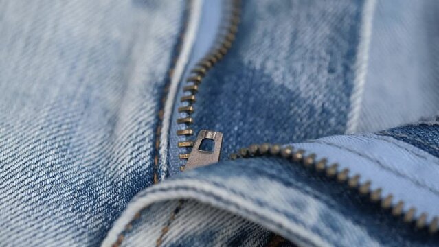 closeup unbuttoned zipper on jeans. rotating the fabric of blue jeans in details. closure, denim texture, abstract background. concept of tailoring.