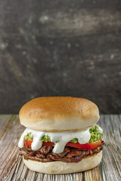 Churrasco italian sandwich popular in chile, round bread, beef, tomato and palta, mayonnaise, on wooden table, vertical, copy space. Typical Chilean food concept