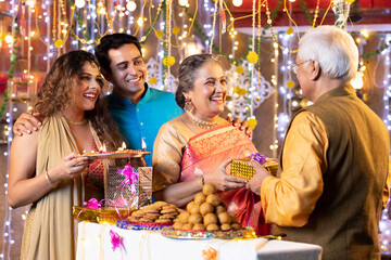 Happy indian family with sweet food and gifts on the occasion of Diwali festival celebration at home.