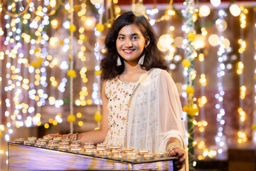 Girl with diya illuminated home during diwali festival.