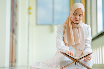 The image of an Asian Muslim woman in the Islamic religion in hijab in cream color. reading the...