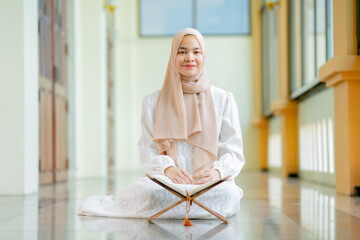 The image of an Asian Muslim woman in the Islamic religion in hijab in cream color. reading the...