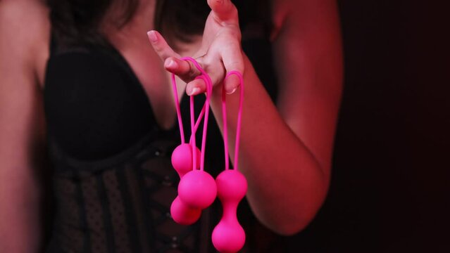 Woman's hand holds pink Kegel balls, Ben Wa balls on a black isolated background. Vaginal balls in a woman's hand. Sex toys Geisha balls. Sex shop. Girl in sexy lingerie
