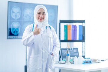 Fototapeta premium Medical Hospital Portrait: Confident female muslim doctor sitting at office desk and smiling at the camera, health care and prevention concept