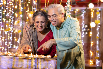 Happy Senior couple decorating with Diya on the occasion of Diwali festival celebration.