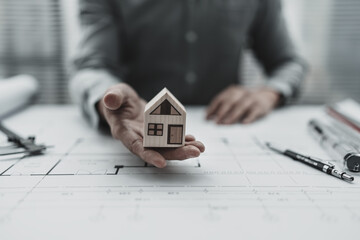 Architect engineer hands hold and protect mini house model on blueprint.  Sell, Protect House, cost planning design and construction concept. - Powered by Adobe