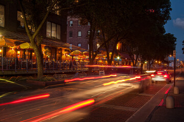 night time on a busy street with restaurants and cars passing by leaving light trails