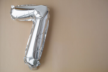 7 seven metallic balloon on beige neutral background. Greeting card silver foil balloon number Happy birthday holiday concept. Copy space for text. Celebration party congratulation decoration