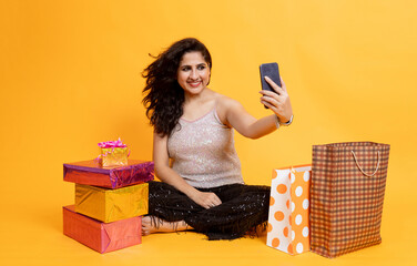 Indian girl with shopping bag and gift box sitting on floor taking selfie , Festive season shopping...