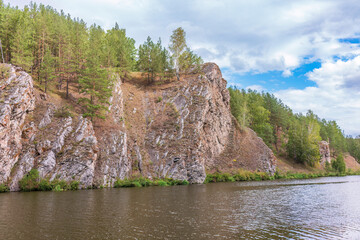 Pine trees and rocks on the river shore with fall foliage around