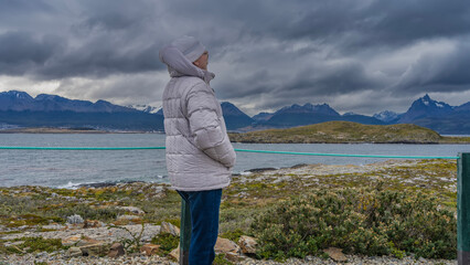 A man in a down jacket and a hat is standing on an island in the Beagle Channel, looking into the...