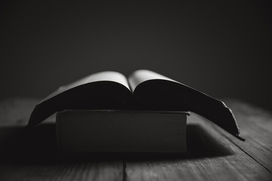 open Holy Bible on black. Cross on the Bible on a wooden background. Holy book. Black and white photography.