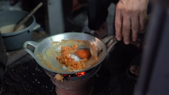 Kerak Telor is a traditional food from Jakarta made from duck egg mixed with sticky rice grated coconut. The seller is cooking egg crust or kerak telor in a small wok with a charcoal stove. 