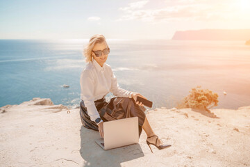 Freelance women sea working on a computer. Pretty middle aged woman with computer and phone outdoors with beautiful sea view. The concept of remote work.