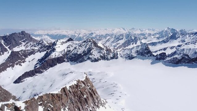 Beautiful cinematic aerial of snowy alpine mountain glacier peaks. Valleys and steep snow covered mountain ranges in distance. Drone flying forward, sunny day amazing landscape scenery view 4K