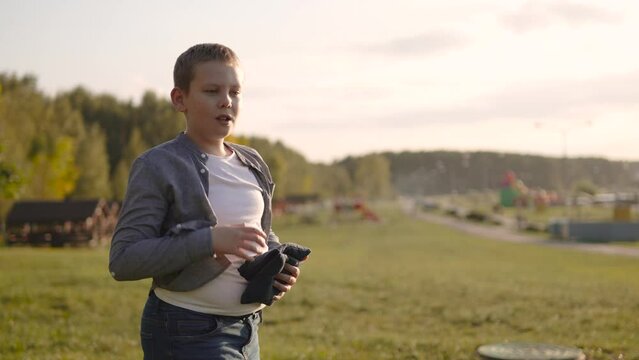 Boy plays cornhole, throwing bean bags and reacting emotionally to misses and hits. Game of accuracy competition in sunny weather on lawn. Portrait of diligent overweight child having fun in sunlight.