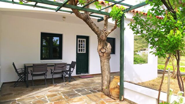 Home house patio garden porch, outdoor dining tables, chairs by trellis gazebo pergola grape, apricot trees in summer on Greek Ikaria Island, Greece