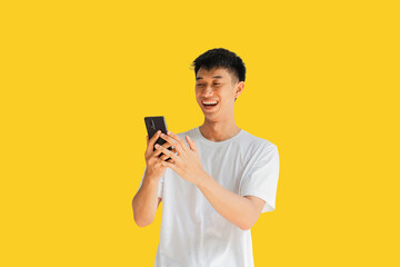 A handsome Asian man wearing a white t-shirt is happily playing on a mobile phone isolated on...
