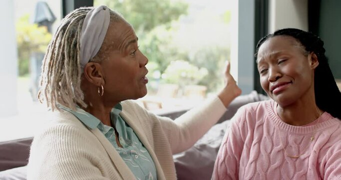 Happy african american senior mother and daughter on couch, talking and embracing, slow motion