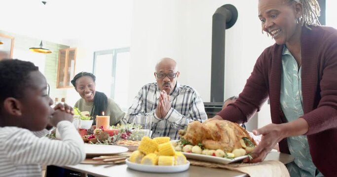 Happy african american multi generation family serving food at thanksgiving dinner, slow motion