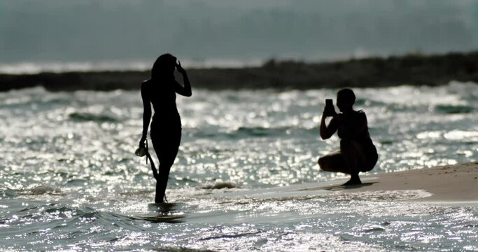 Silhouette of people taking photos on vacation by the sea. Beautiful waves of the ocean, recreation, tourism. High quality 4k footage