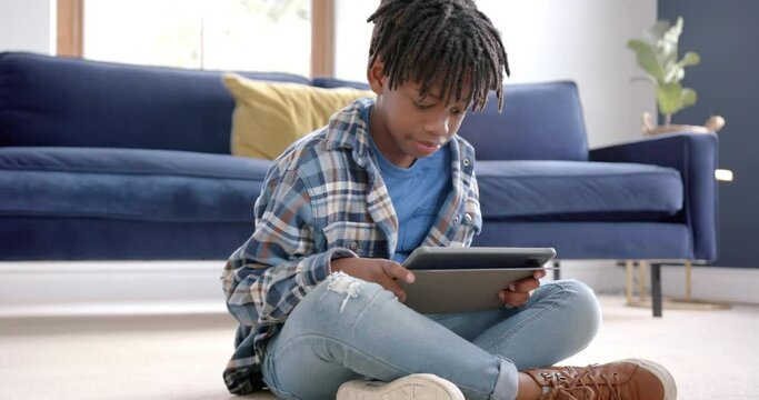 African american boy using tablet sitting on floor at home, slow motion