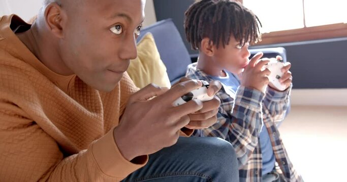 African american father and son playing video games at home, slow motion